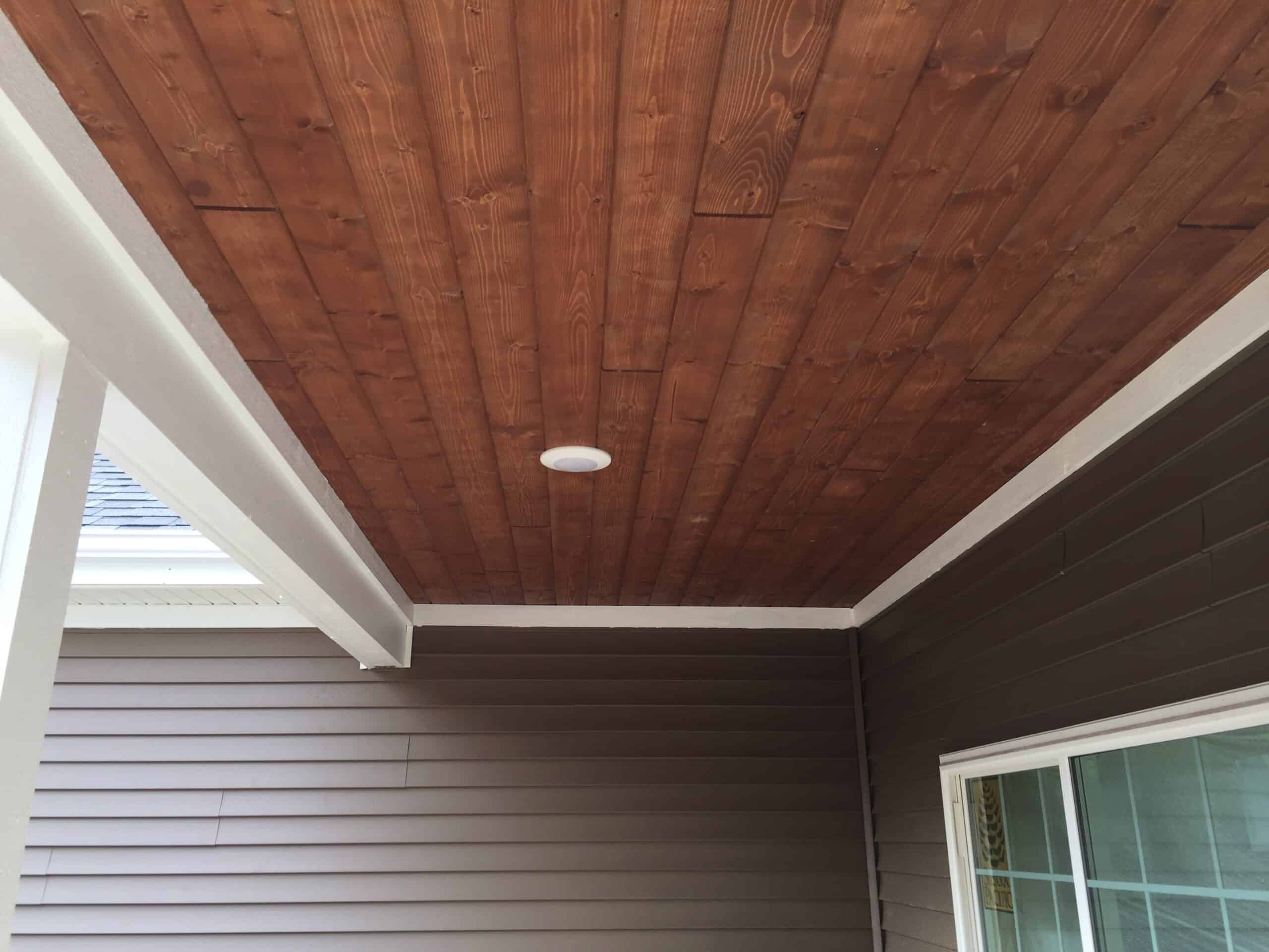 A porch exterior with brown horizontal siding and warm-toned tongue-and-groove ceiling panels.