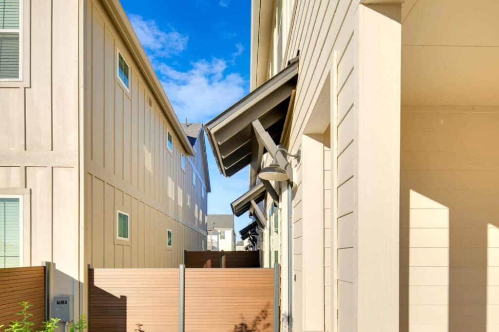 Narrow walkway between modern residential buildings showing exterior siding and trim installation.